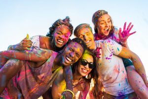 happy young multiethnic friends with colorful paint on clothes having fun together at holi festival