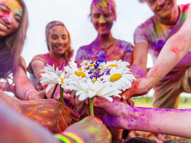 cropped shot of young friends holding chamomiles at holi festival