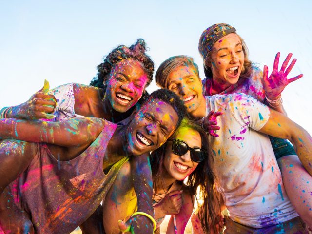 happy young multiethnic friends with colorful paint on clothes having fun together at holi festival